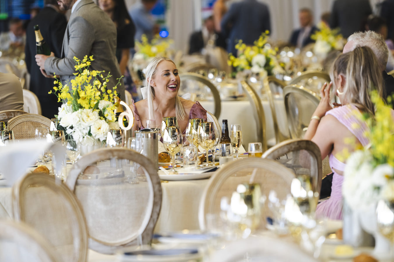 A woman laughs while seated at an ornately decorated table within a racecourse function space